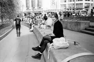 Kuvassa Annukka istuu kadun reunuksella kaupungin keskustassa.