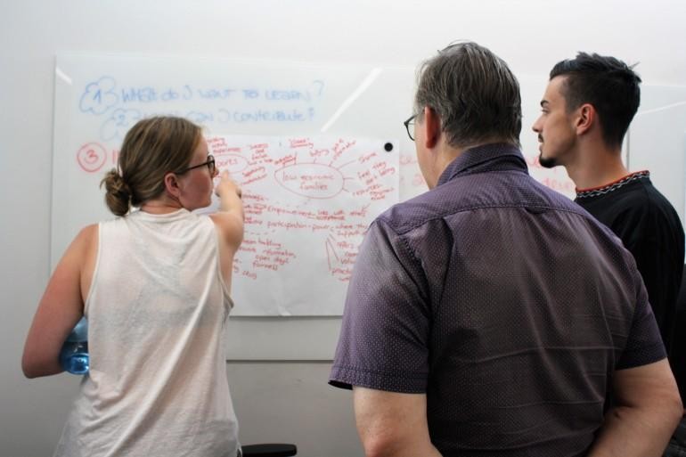 People looking at a whiteboard, a person showing a part of the text in the board.