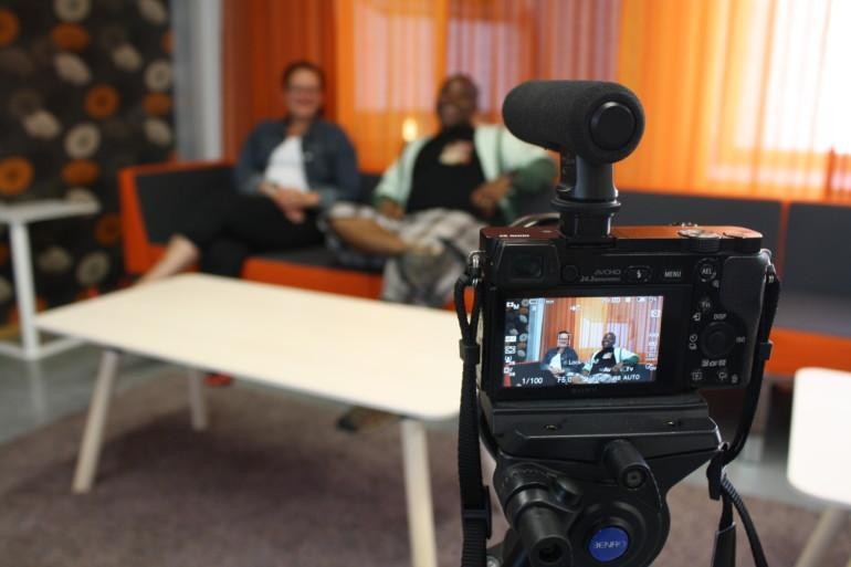 Two people on a sofa, video camera in front of them filming.