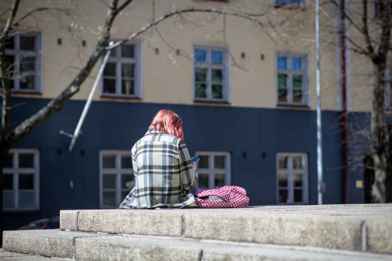 Nuori istuu selkä kameraa kohti, kännykkä kädessään.