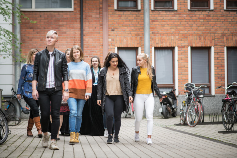 Nuoria opiskelijoita eri kulttuuritaustoista kävelee tiilitalon pihalla. Kuva: Diak.