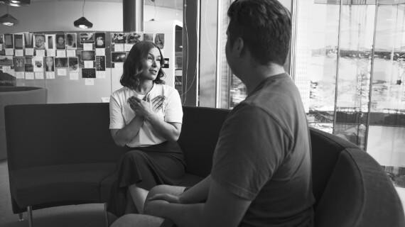 A woman and a man are having a conversation. The woman has her arms crossed over her chest – it is the sign language sign for Diak.