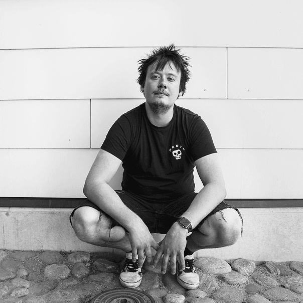 Nuori mies on kyykyssä seinän edessä ja katsoo kameraan. Kuva on mustavalkoinen.