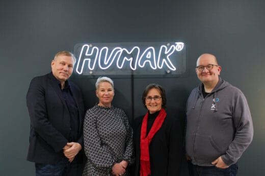 Toimitusjohtaja-rehtorit Jukka Määttä Humakista, Kati Komulainen Diakista, Mona Forsskål Arcadasta ja Matti Sarén KAMKista poseeraavat yhdessä HUMAKin valokyltin edessä tummanharmaata seinää vasten.