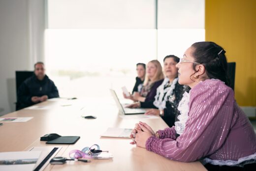 ihmisiä ison pöydän äärellä.kaksi naista kannettavan tietokoneen äärellä.kaksi romaninaista kirjastossa.