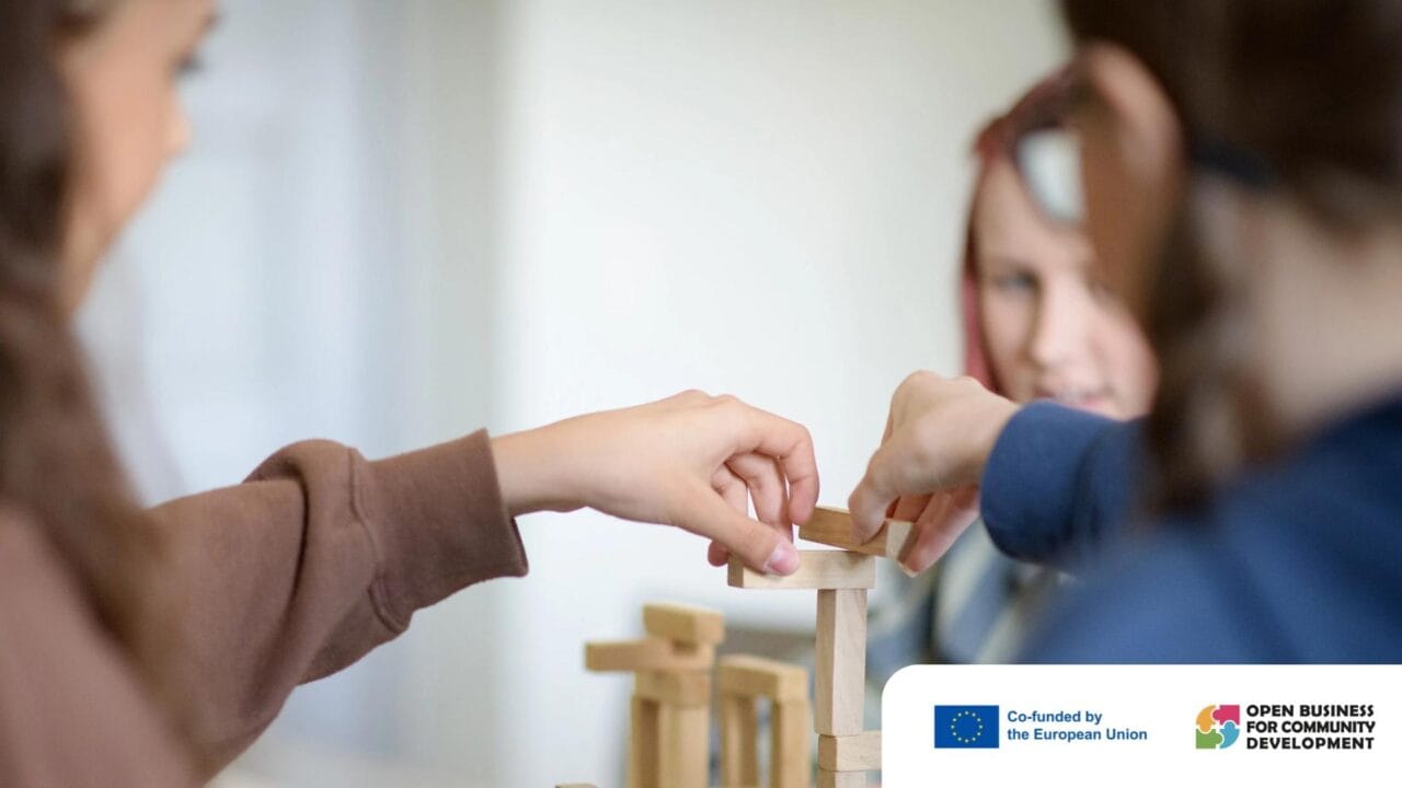 Kaksi henkilöä rakentaa puupalikoista tornia. Kuvassa näkyy kaksi kättä