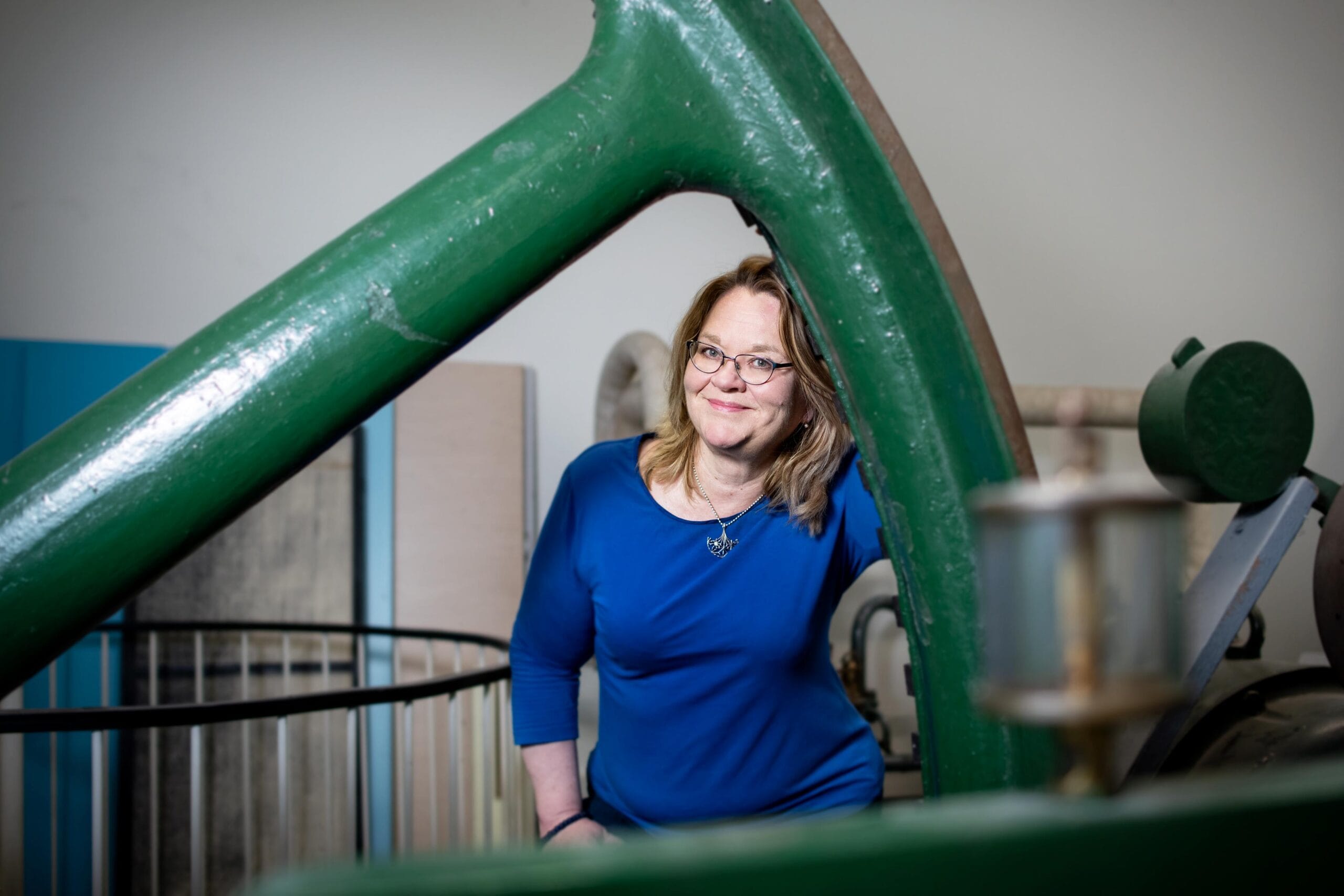 hän pitää käsissään robottinukkea.Christina Andersson hymyilee ja ottaa hyllyltä pientä robottileluaLasipöydällä rivissä robottilelu ja erilaisia robottityövälineitä.