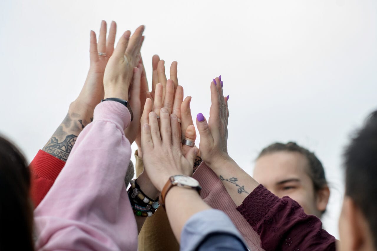 Ryhmä ihmisiä nostaa kätensä yhteen yläviistoon symbolisena yhteishengen ja yhteistyön eleenä.