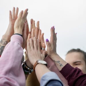 Ryhmä ihmisiä nostaa kätensä yhteen yläviistoon symbolisena yhteishengen ja yhteistyön eleenä.