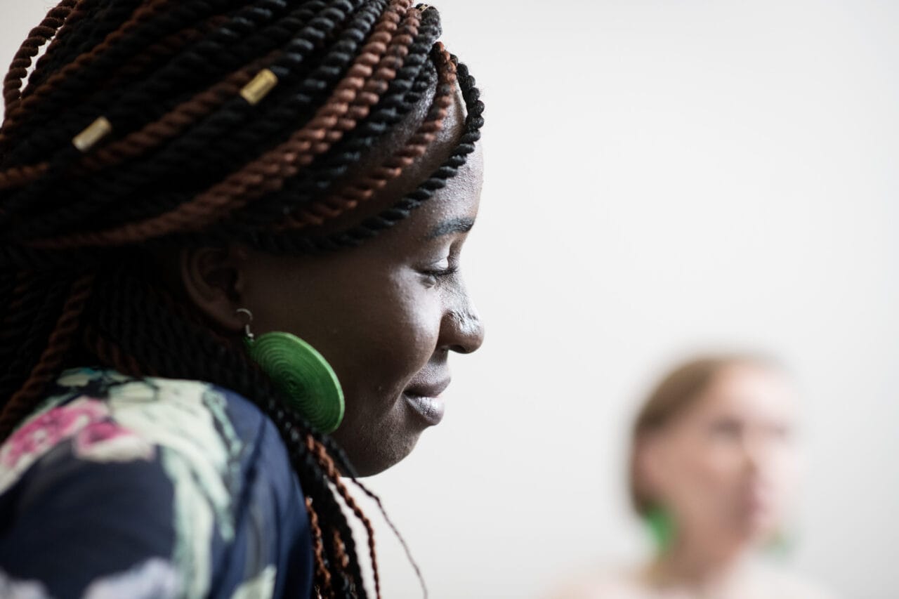 Lähikuva naisesta, joka katsoo sivulle alas. Taustalla toinen henkilö näkyy sumuisena.