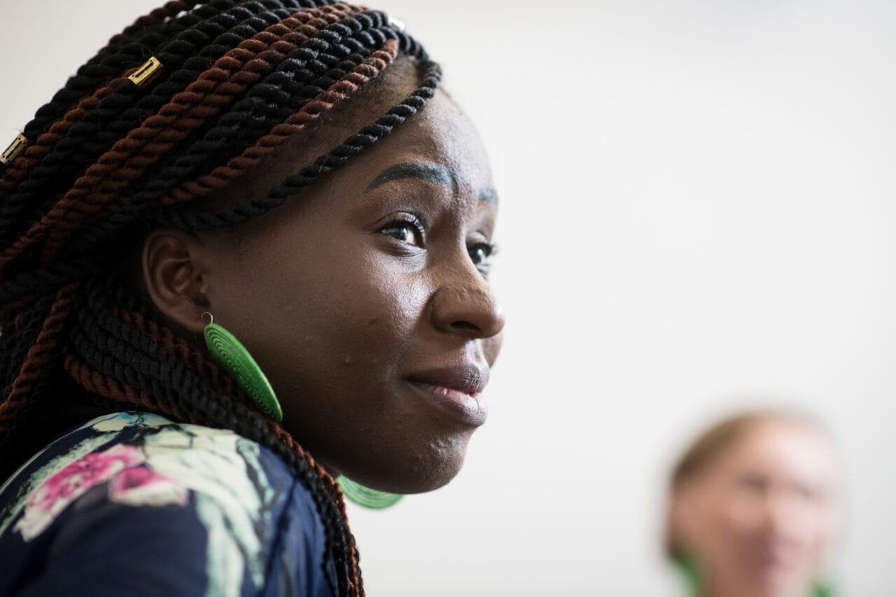 Lähikuva naisesta, joka katsoo ohi kameran. Taustalla toinen henkilö näkyy sumuisena.