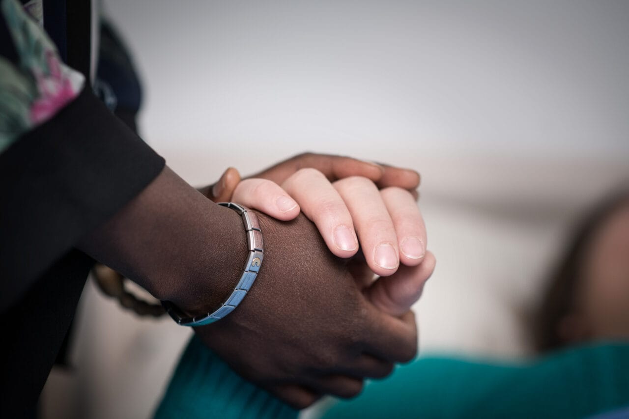 Tummaihoisen naisen käsi pitää vaaleaihoisen naisen kättä.Viittomakieliset opiskelijat keskustelevat.