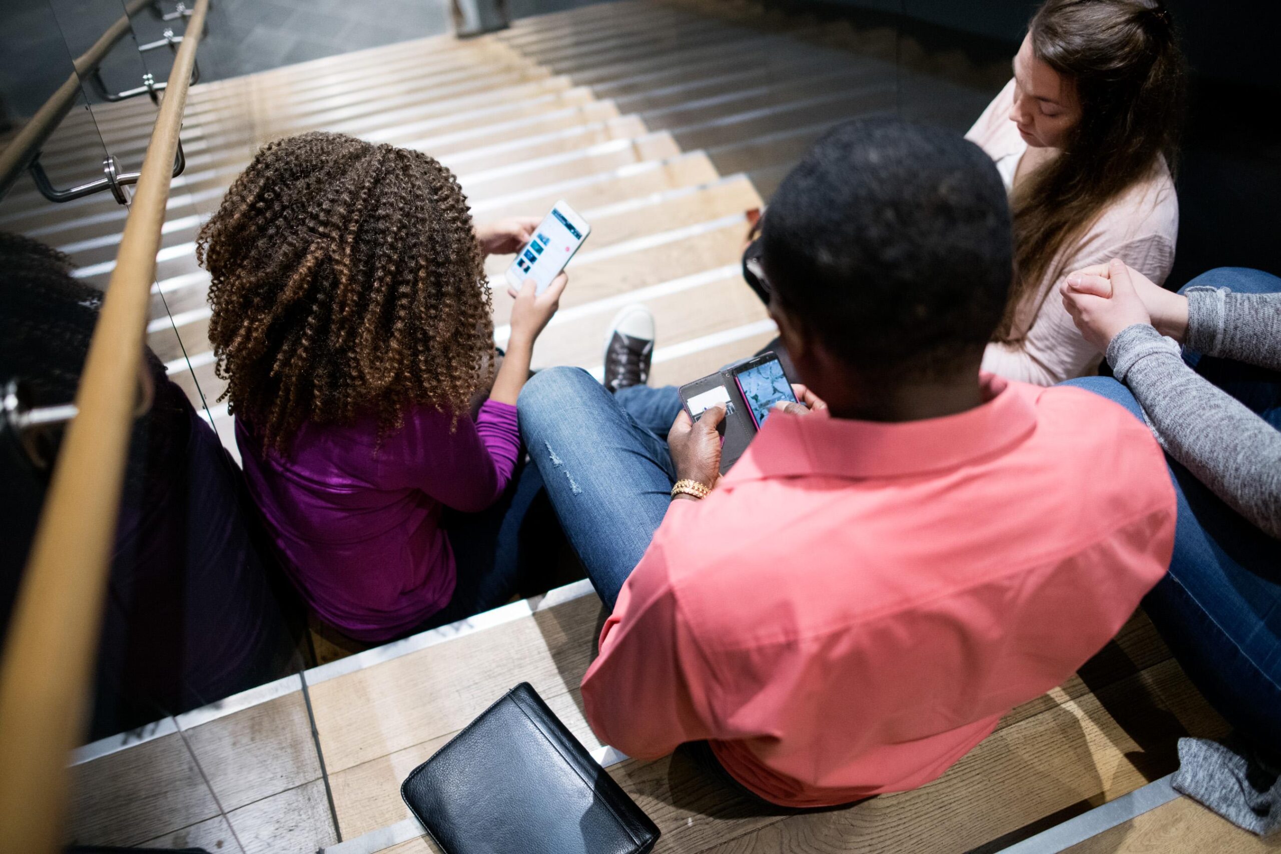 Nuoret istuvat portailla ja katsovat puhelimiaan.