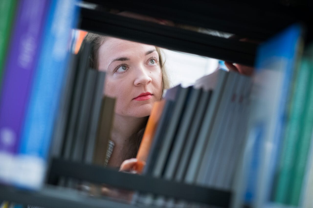 Nainen kuvattuna kirjahyllyn välien välistä.