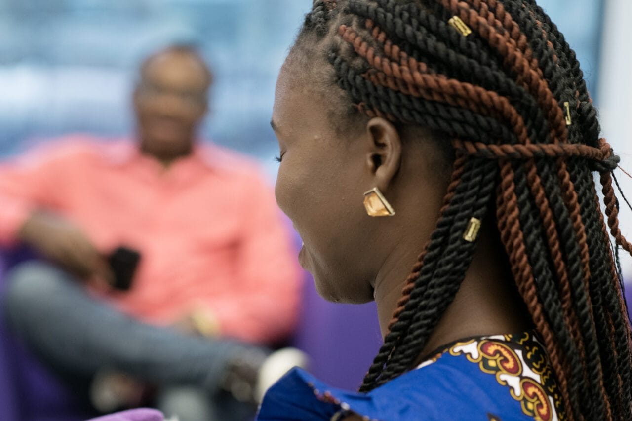 Etualalla on nainen joka on kuvattu takaapäin. Hän hymyilee. Taustalla sumuinen mies, joka myös hymyilee.