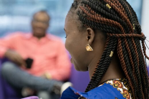 Etualalla on nainen joka on kuvattu takaapäin. Hän hymyilee. Taustalla sumuinen mies, joka myös hymyilee.