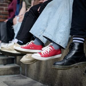 Ulkona korokkeella nuoret istuvat rivissä ja heidän jalkansa ovat kuvassa.