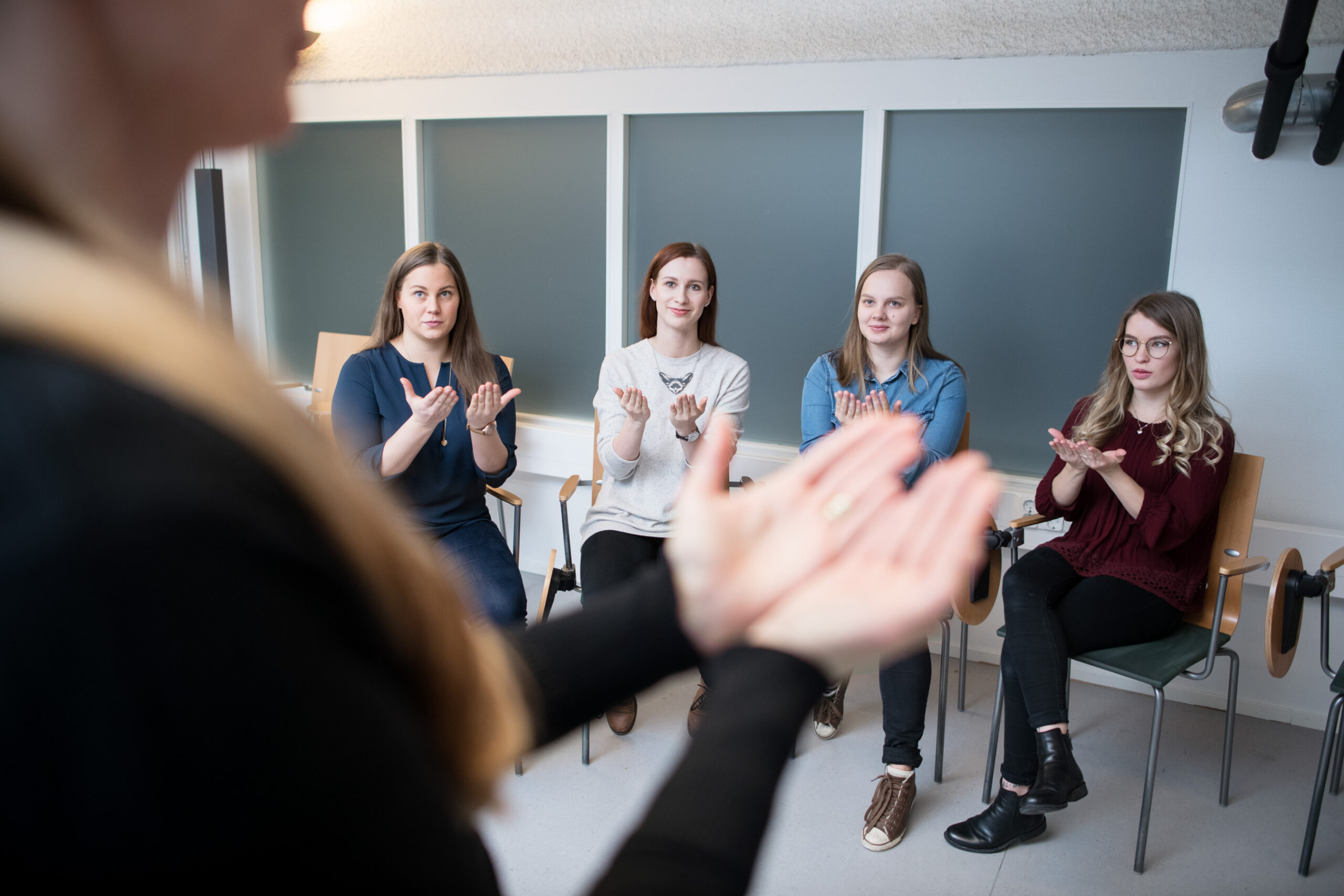 Nuoria ihmisiä ringissä lattialla.Tietokone sylissä oleva ihminen.Pulssia mittaava sairaanhoitaja ja potilas.Opettajalla kädet auki