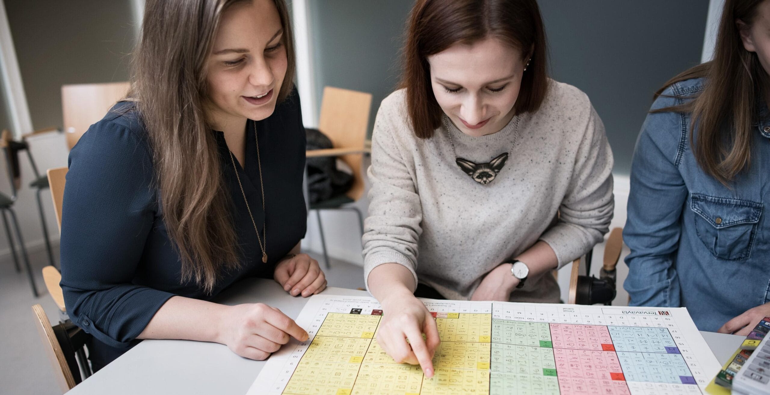 Opiskelijat tutkimassa bliss-kuvia.Bliss-symbolikuvaa osoittavat opiskelijat.Kuva käsistä pöydän ääressä.