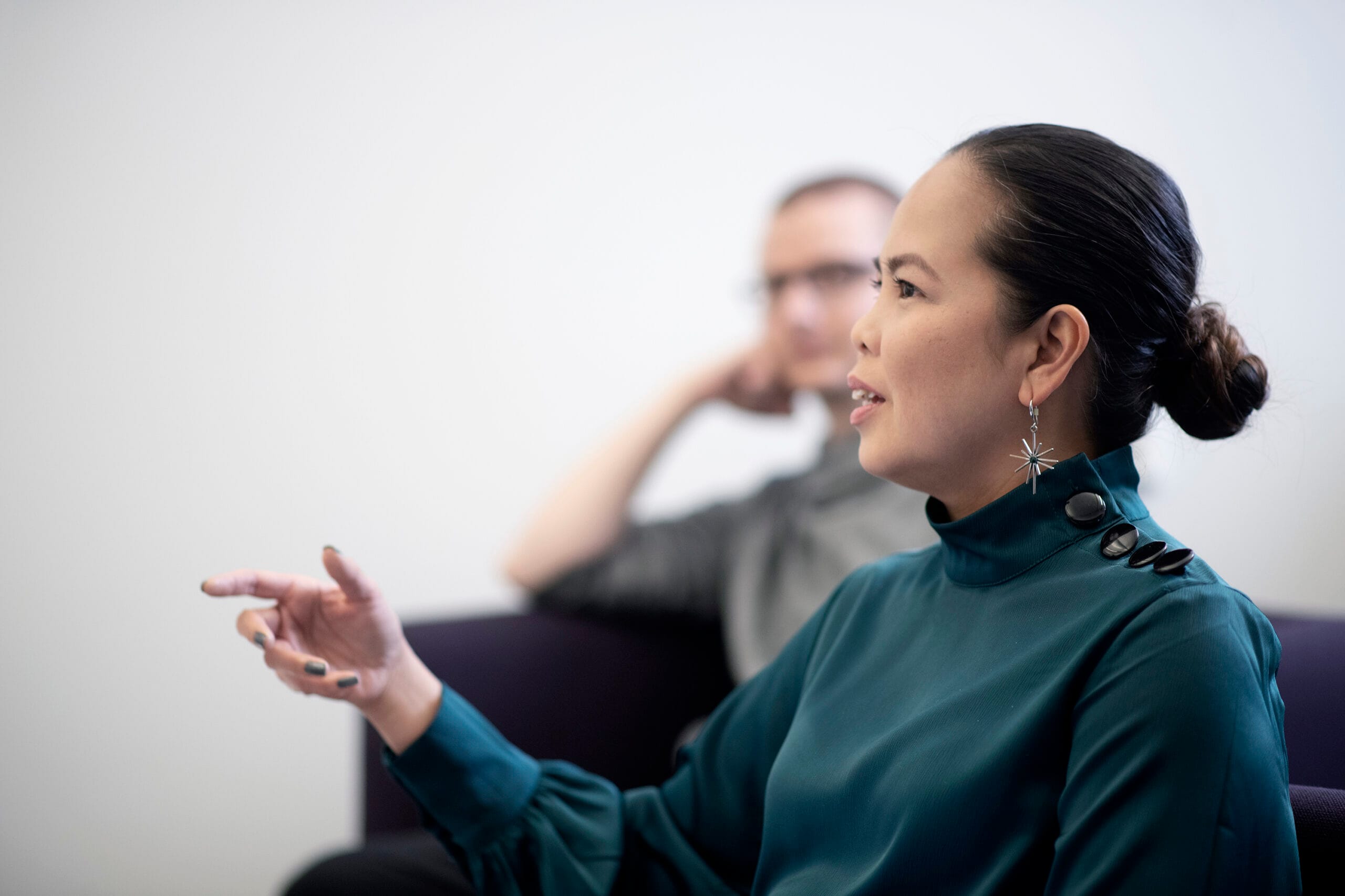 Nainen puhuu ja heiluttaa kättä, taustalla mies. Kuvituskuva.