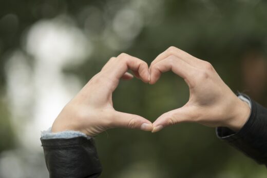 yksi taluttaa polkupyörää.kaksi henkilöä kahvilapöydän ääressä ulkona.naurava nainen katsoo selin olevaa naista.kädet muodostavat sydämen.