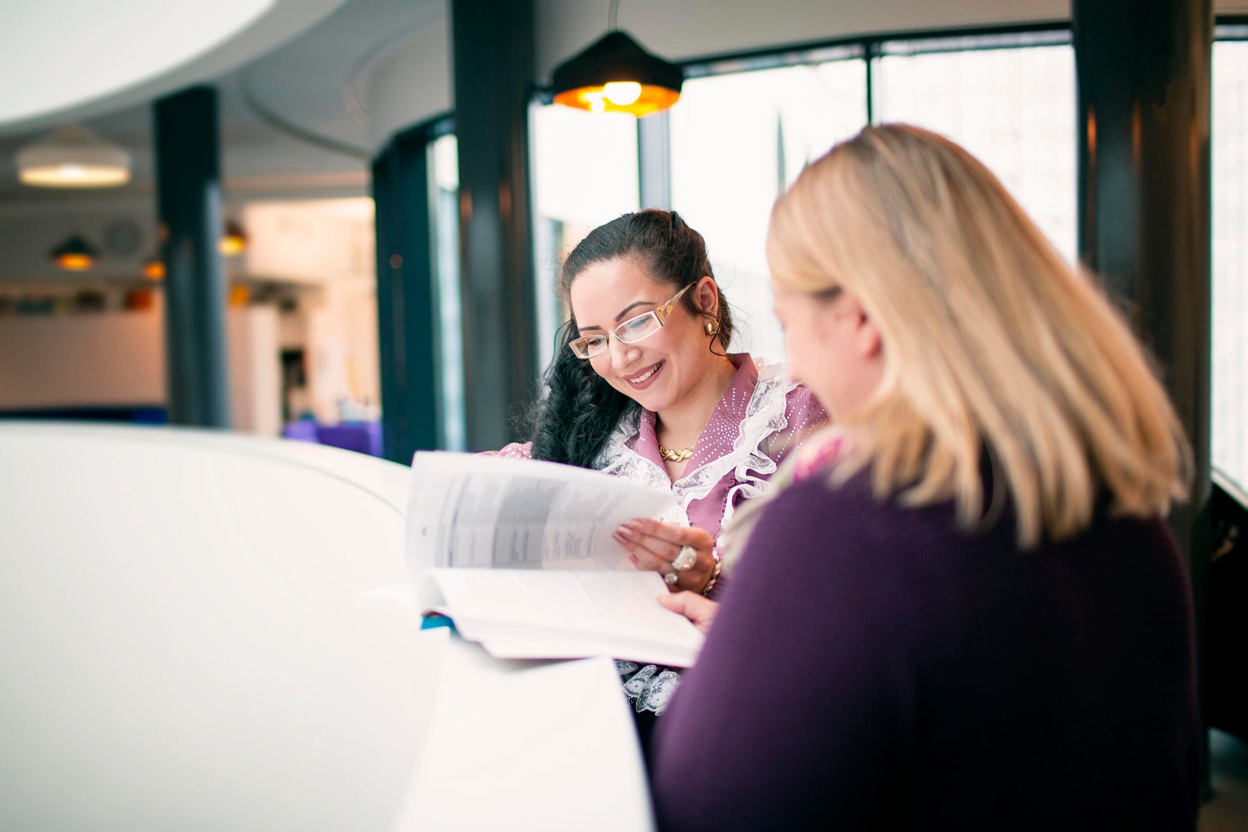 kaksi henkilöä tutkii kirjaa kaiteen vieressä.