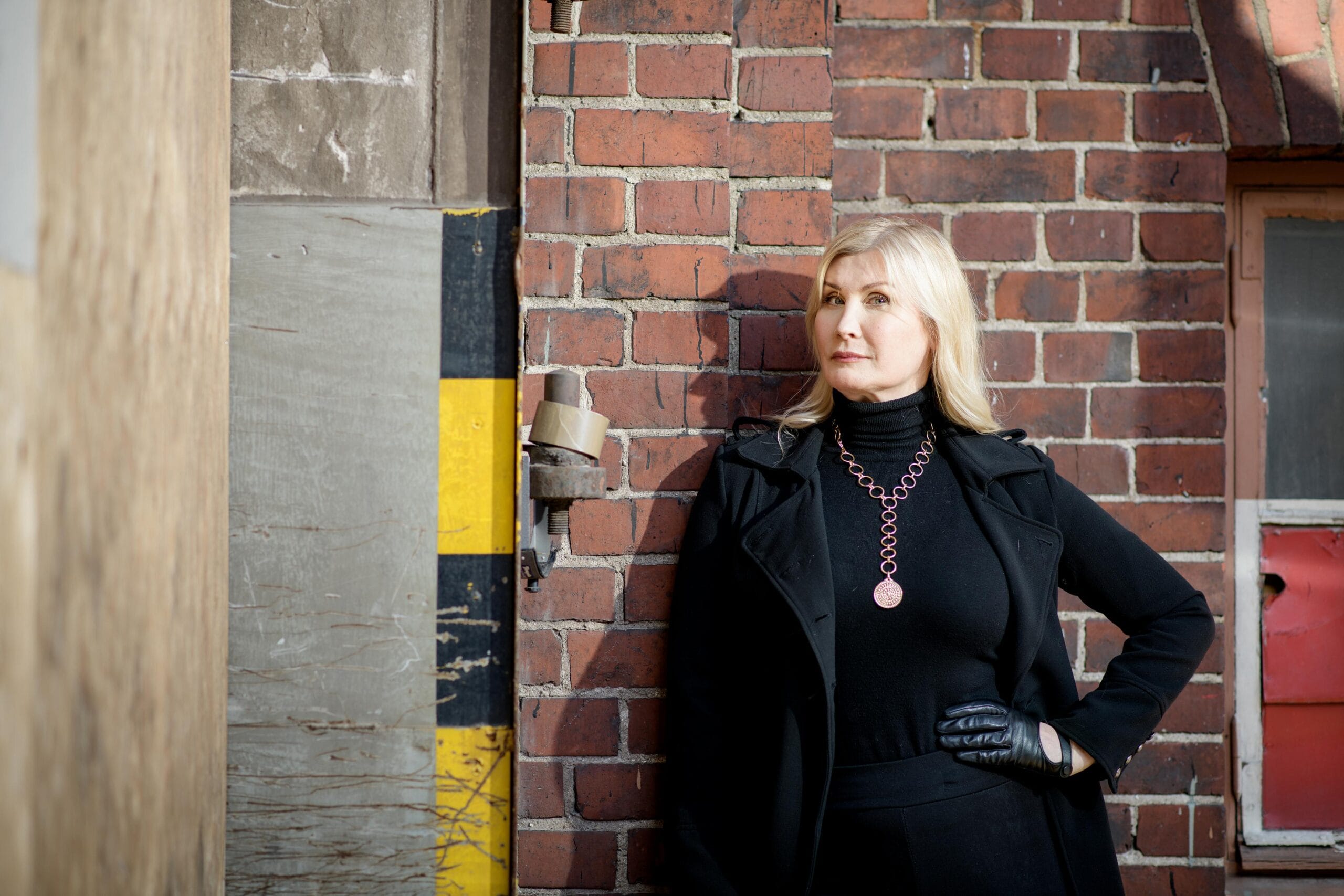 Julia Suikki poseeraa tiiliseinänen edessä.