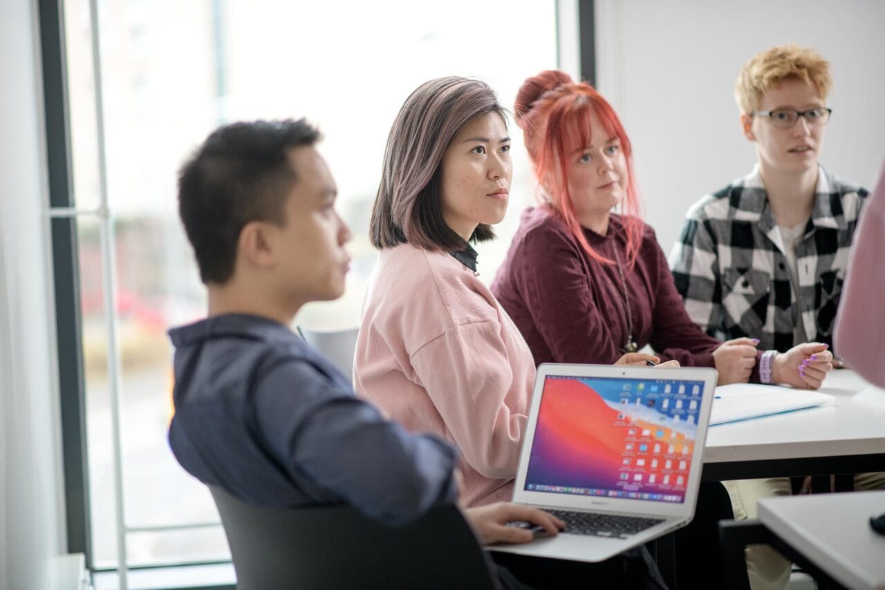 Ryhmä erinäköisiä opiskelijoita kuuntelemassa keskittyneen näköisinä.