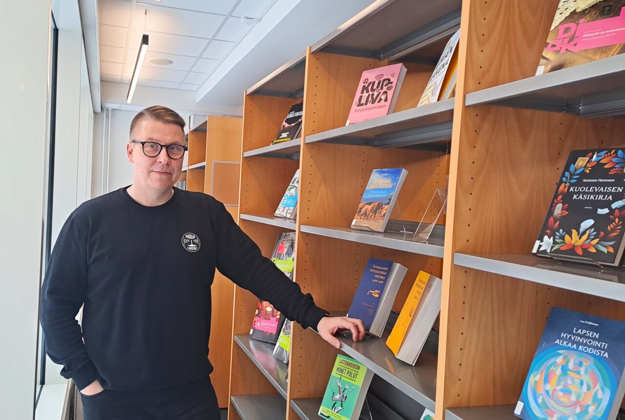 Diakin mustapaitainen miesopiskelija seisoo kirjastossa.