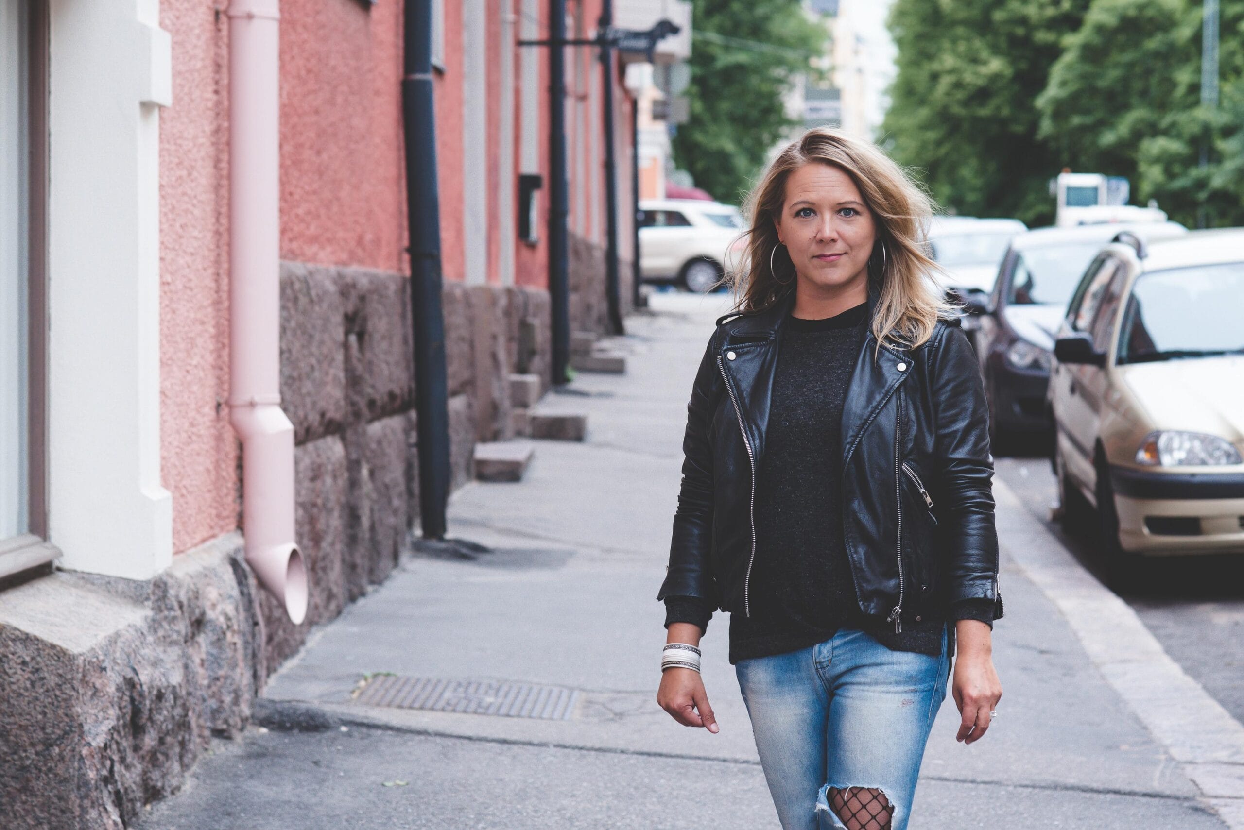 Satu Sutelainen nojaa rakennuksen seinää vasten.Satu Sutelainen seisoo huonekasvin vieressä