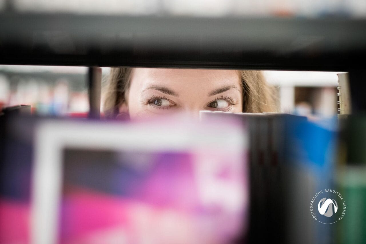 Hyllyn välistä näkyvät naiset silmät.