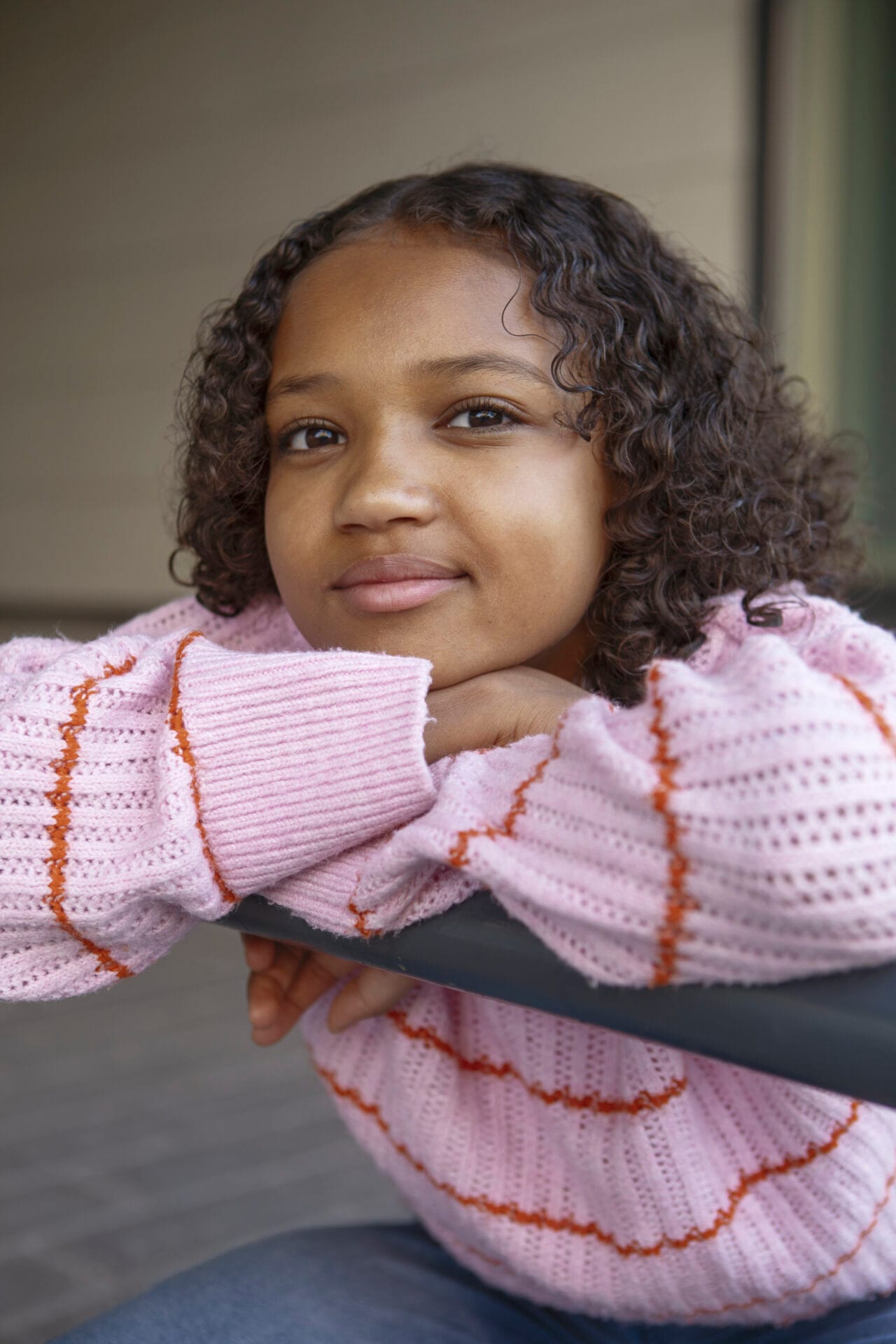Tyttö nojaa kaiteeseen ja hymyilee kameraan muotokuvassa. Yllään vaaleanpunainen neule, taustalla vaalea seinä.