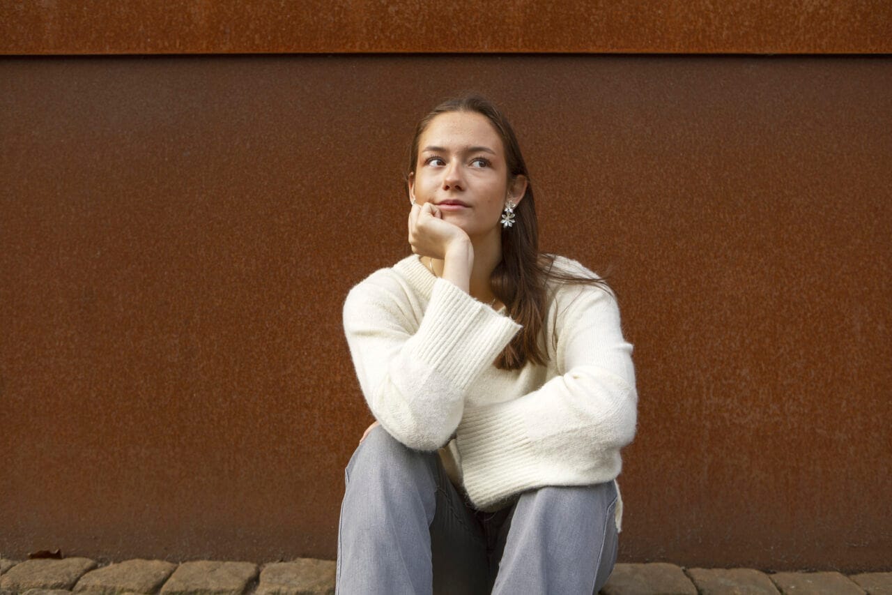 Tyttö istuu maassa ja hänellä on haaveileva katse.