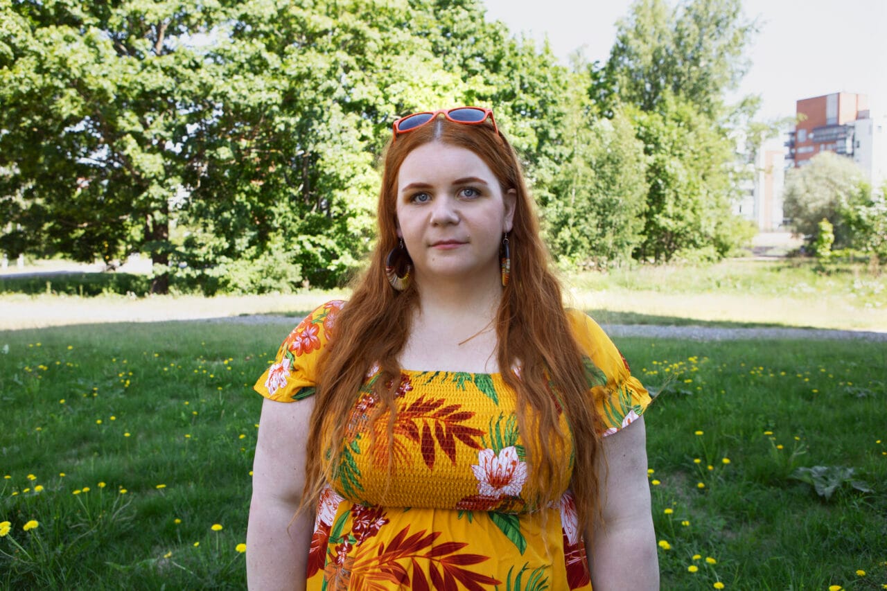 Kukkamekkoinen nainen seisoo nurmikolla.