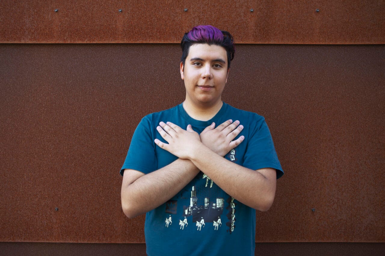 Nuoren miehen kädet ristissä rinnallaan sinisessä paidassa.