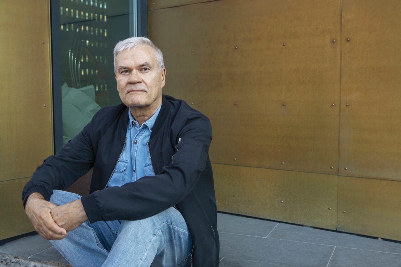 Vanhempi mies istuu rappusilla ja katsoo kameraan.