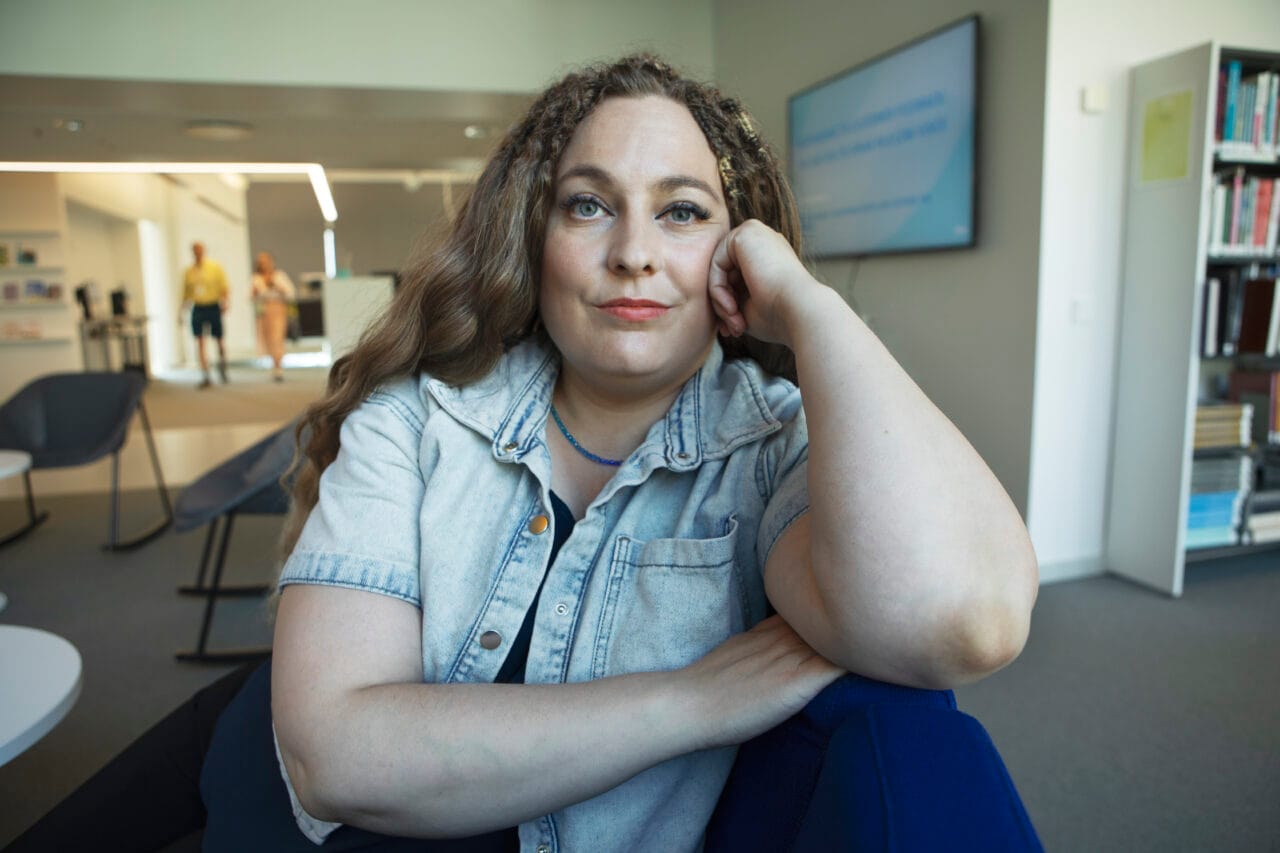 Nainen nojaa käsivarteensa ja katsoo kameraan kampusympäristössä.