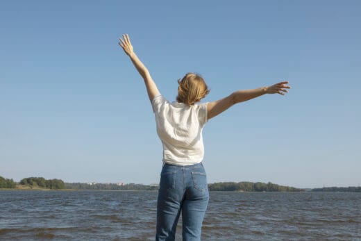 Ulkona meren edessä otettu kuva henkilöstä, jolla on kädet rennosti ylhäällä.