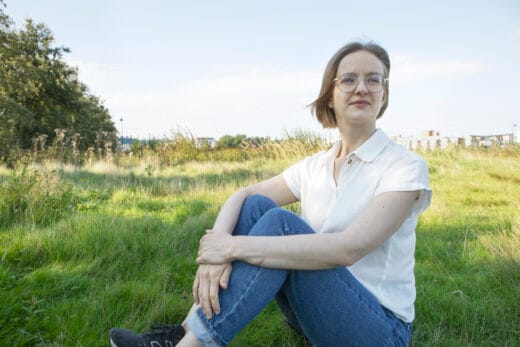 Nainen istuu nurmikolla kesäisessä maisemassa.