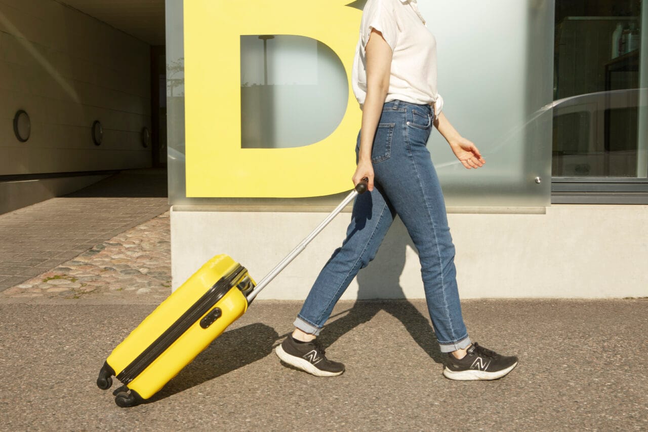 Keltainen matkalaukku ja naisen jalat kävelyssä ulkona.