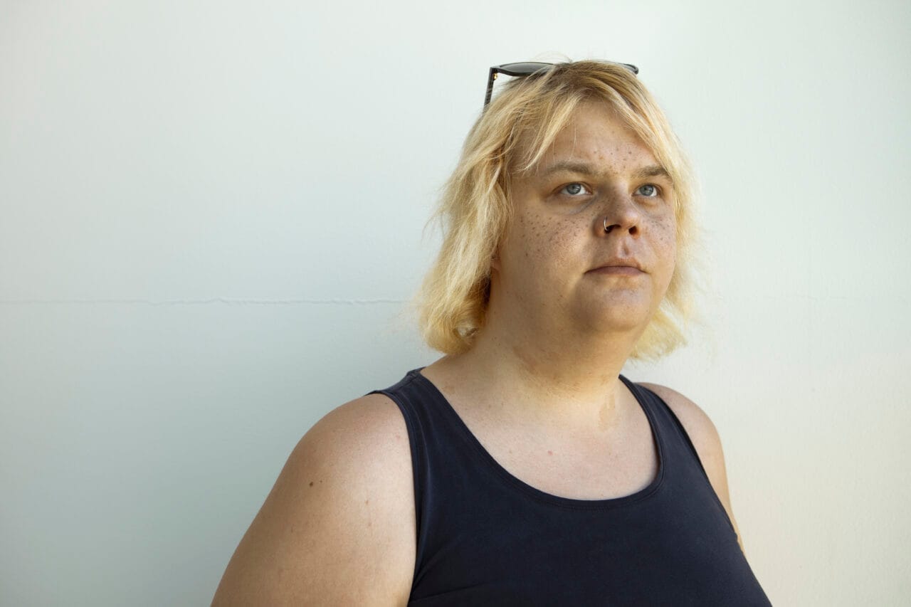 Henkilö seisoo vaaleaa seinää vasten sisätilassa.