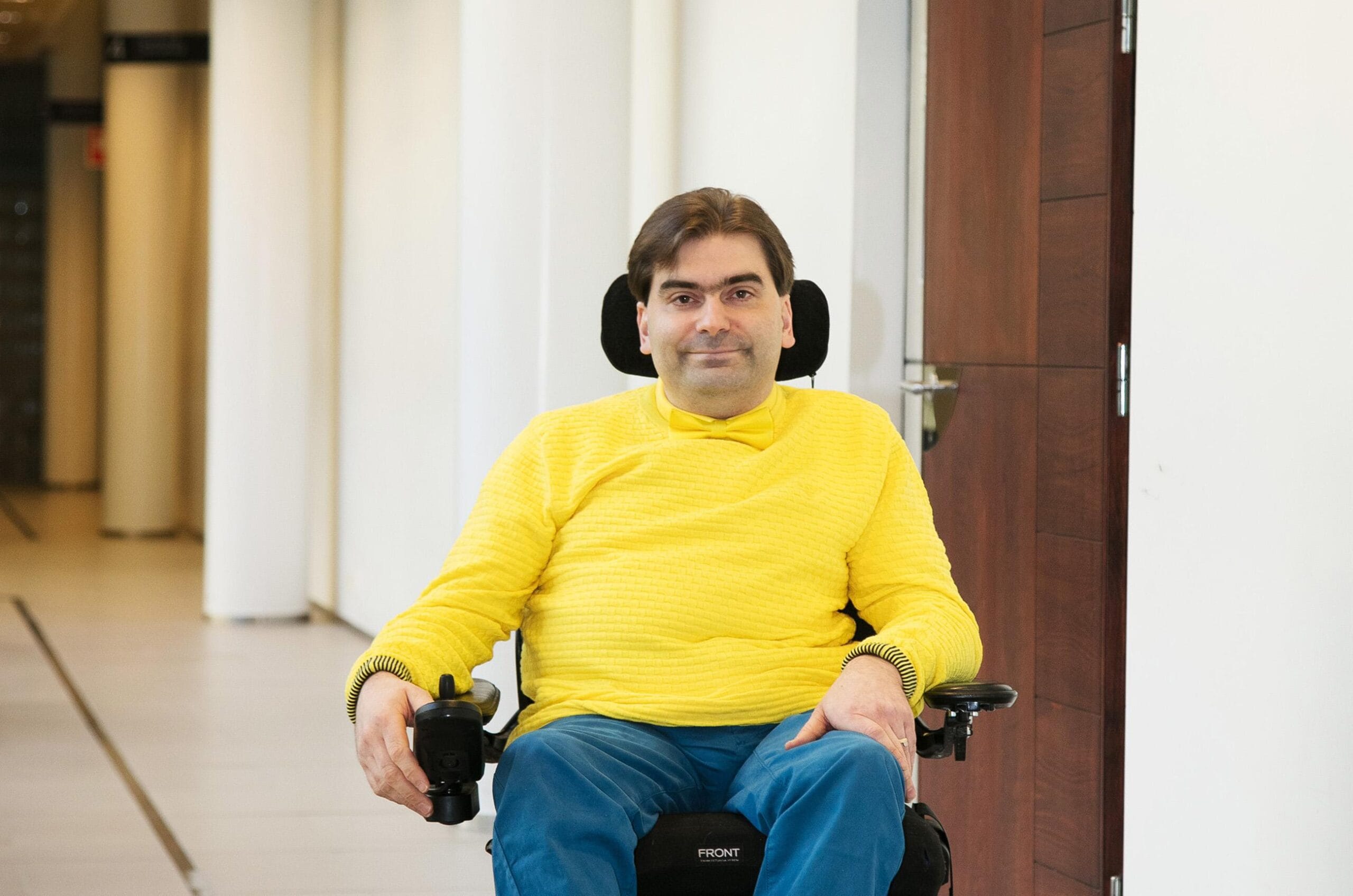 Jukka Kumpuvuori pyörätuolissa.Jukka Kumpuvuori osoittaa invalidikylttiä ulkona.