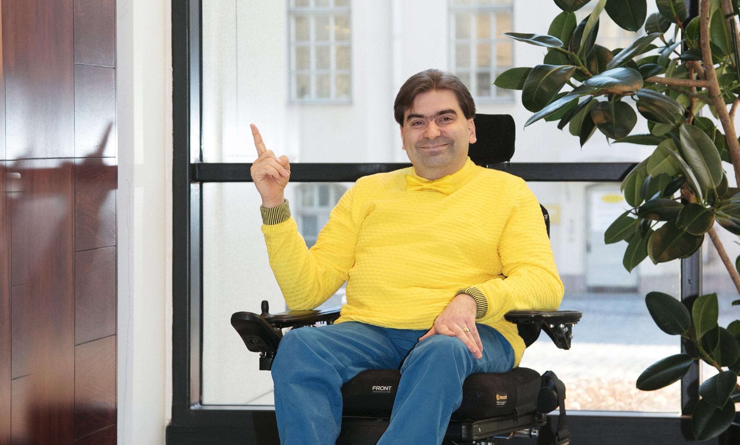 Jukka Kumpuvuori toimistossa, osoittaa sormellaan ylöspäin ja hymyilee.