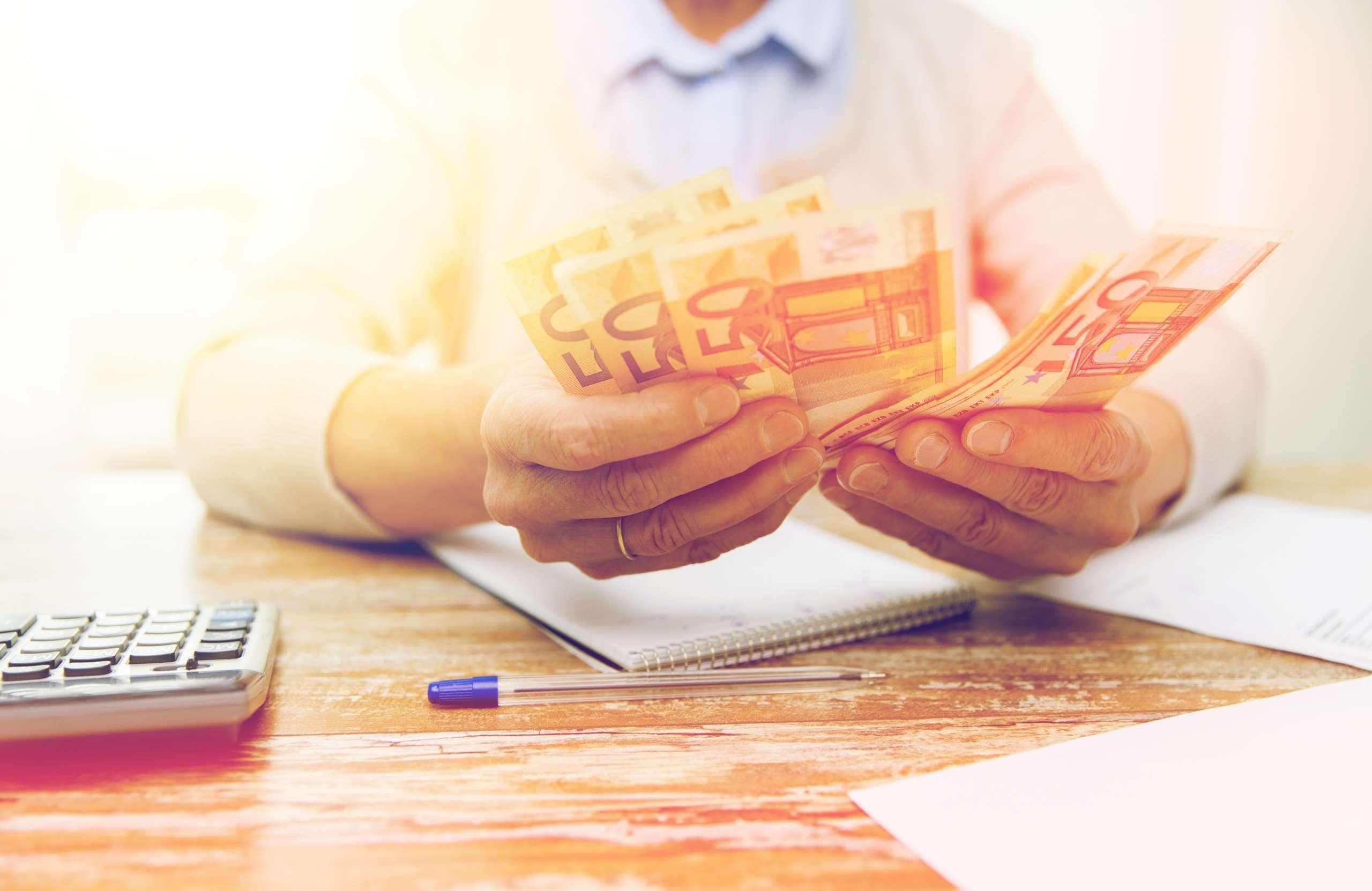 Rahoja pöydän ääressä istuvan henkilön käsissä.