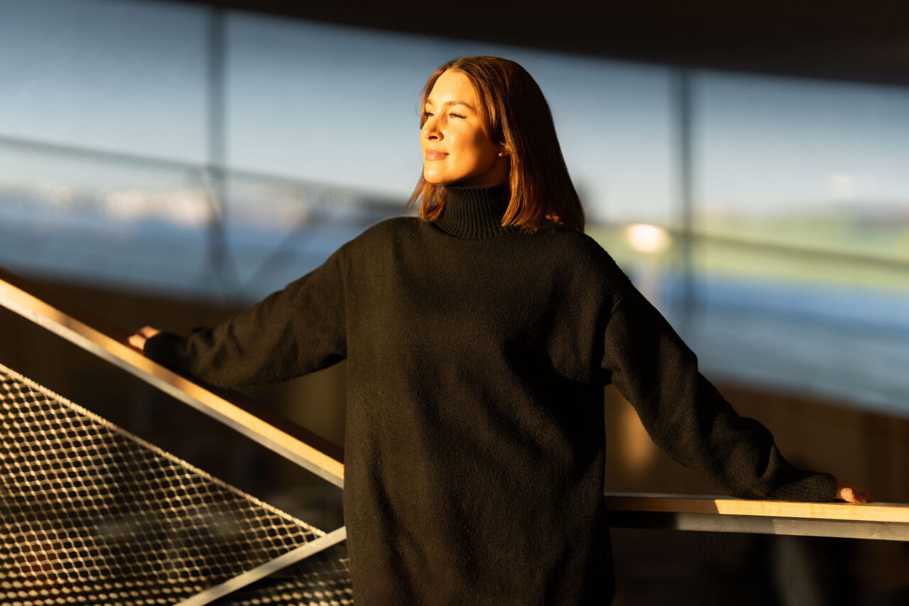 Henkilö seisoo kirjaston portaikossa ja aurinko paistaa hänen kasvoilleen.