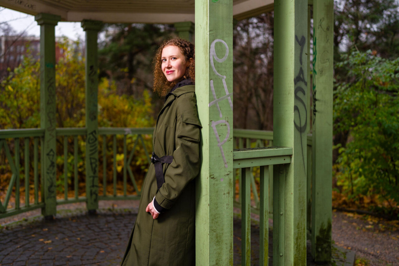 Nainen nojaa vihreään rakennukseen ulkona.