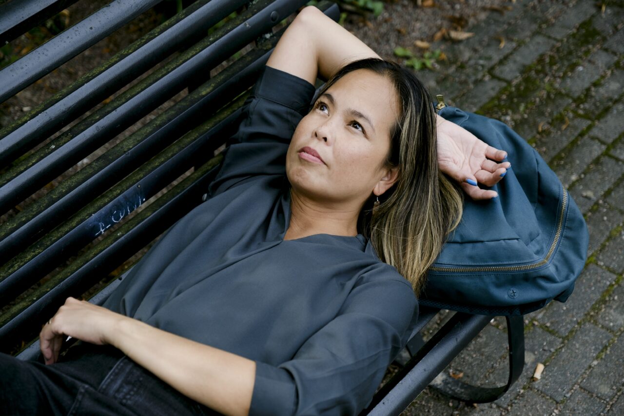 Nainen makaa puiston penkillä ja katsoo ylöspäin.