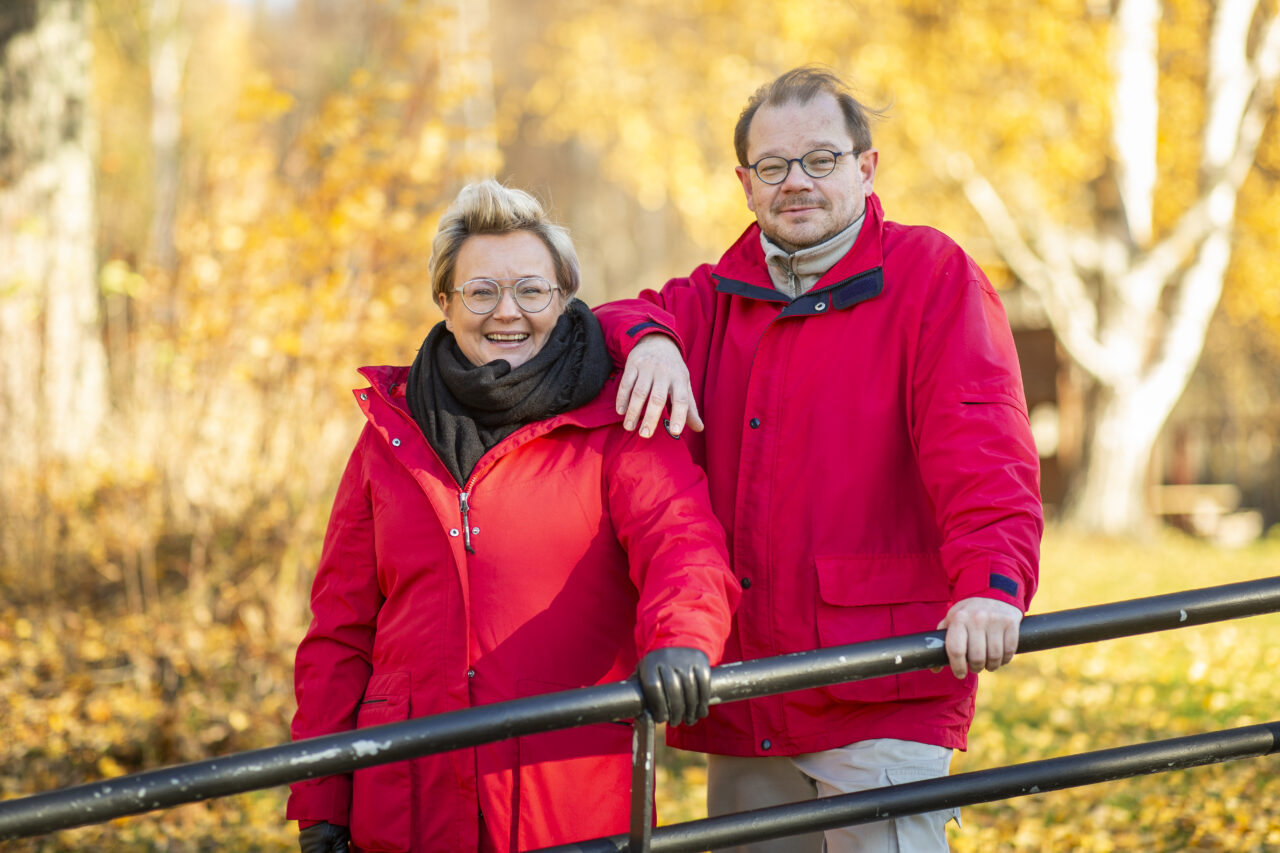 Kaksi puna-asuista henkilöä seisovat vierekkäin syksyisessä maisemassa.