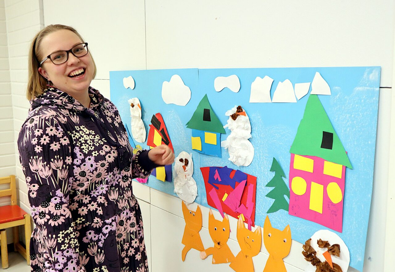 Nainen osoittaa lasten tekemää piirustusta hymyillen.