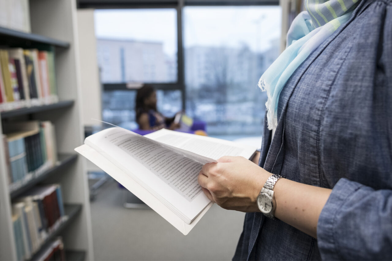 Nainen selailee kirjaa kirjastossa